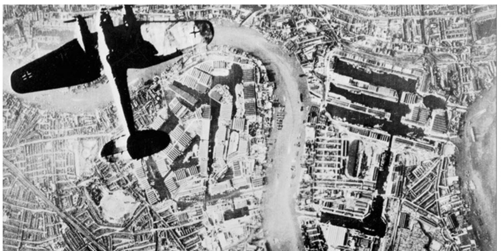 Black and white photo from a german plane above another german bomber over docklands in the Blitz